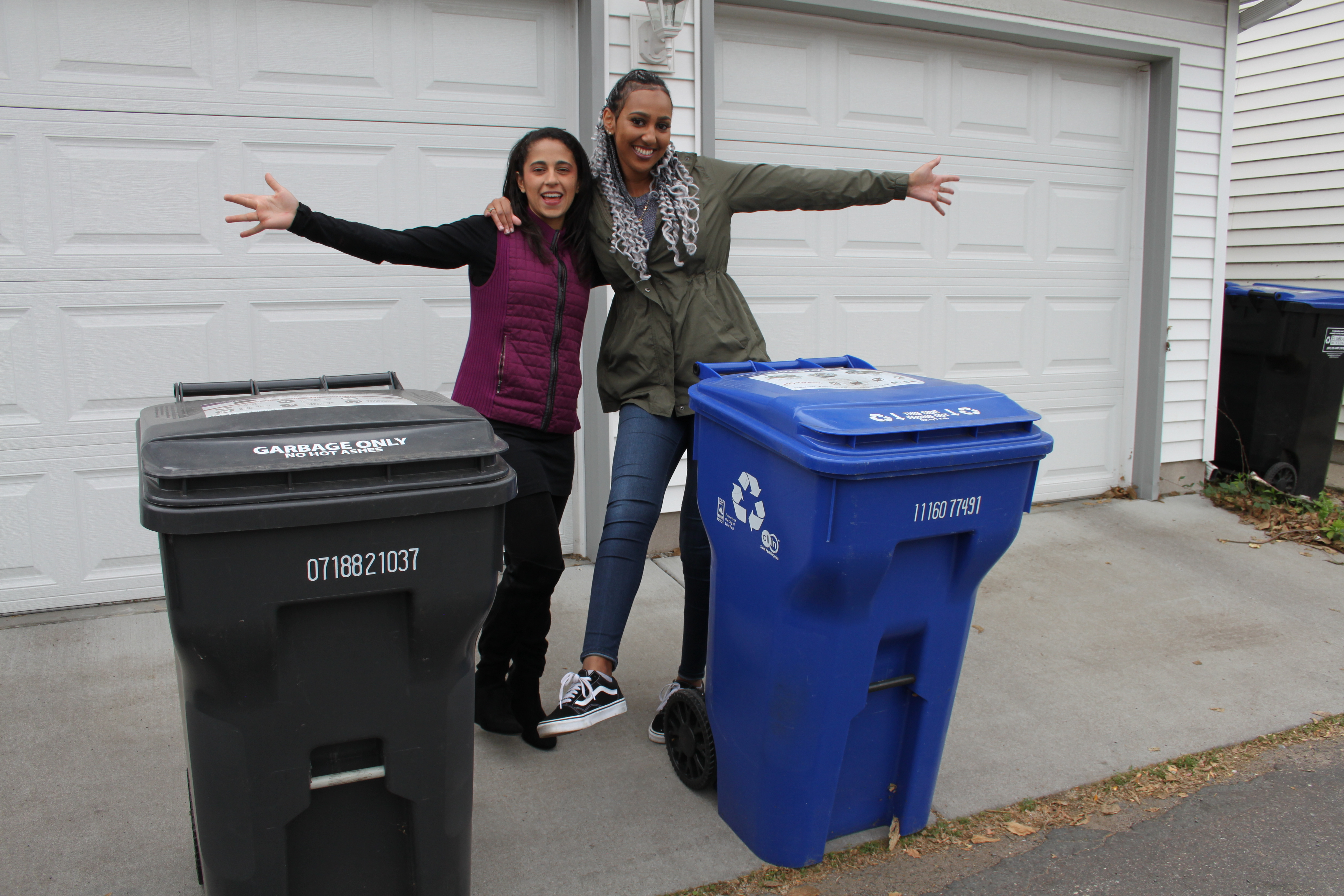 Two women with arms locked next to a garbage and recycling can