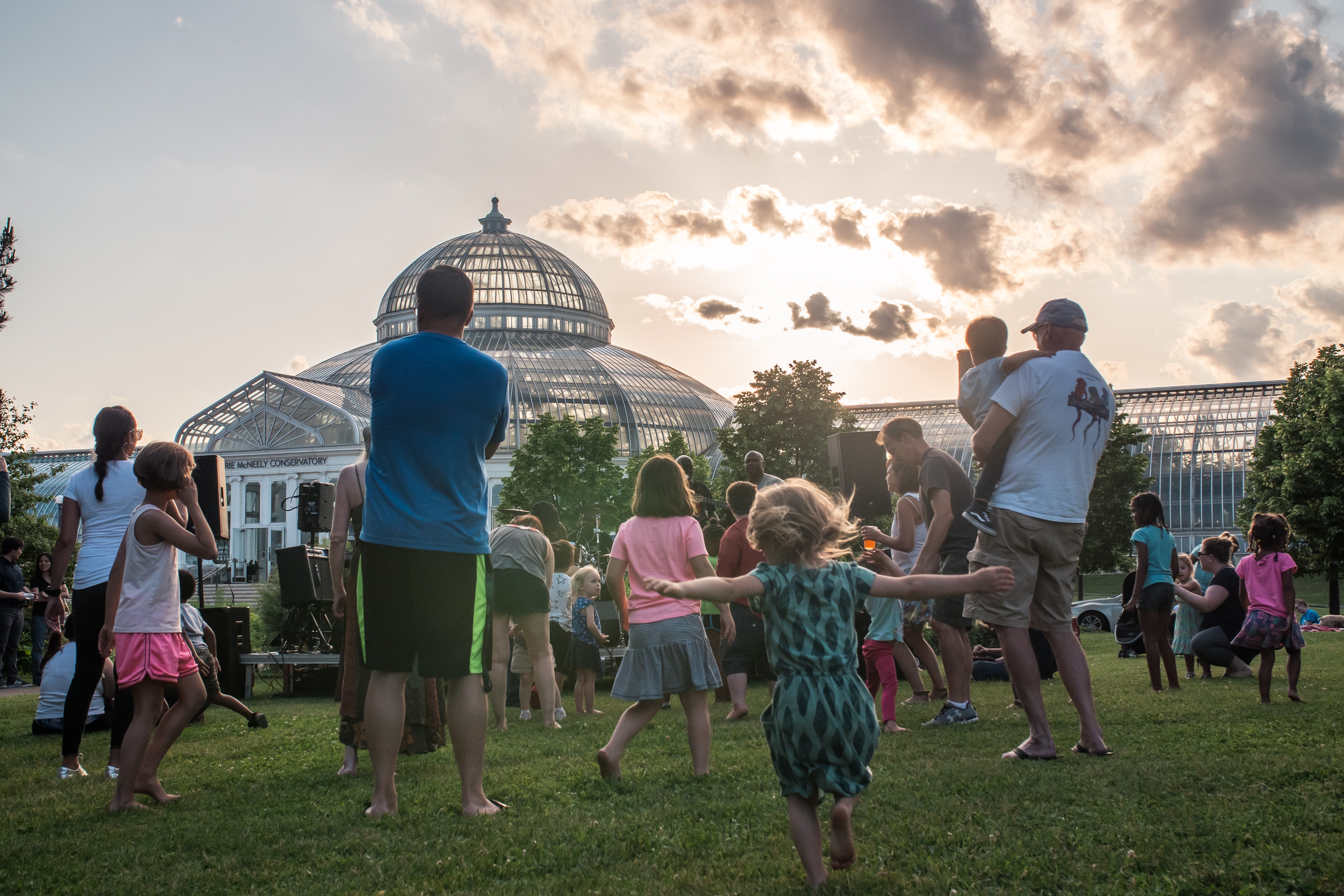 People dance on the lawn in front of a Victorian-era glassouse