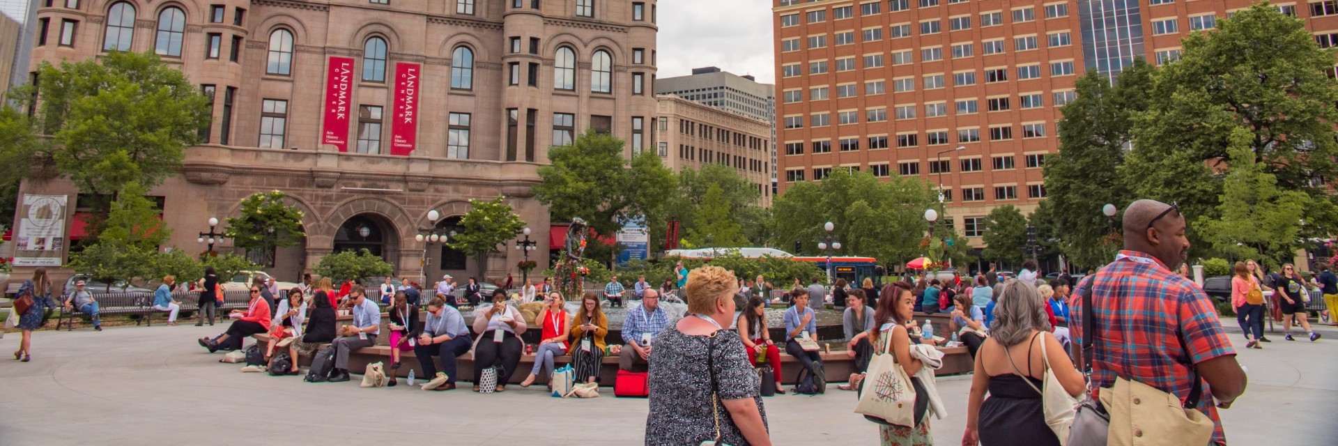 A picture taken in Rice Park. People are seen sitting and walking around the Landmark Center.