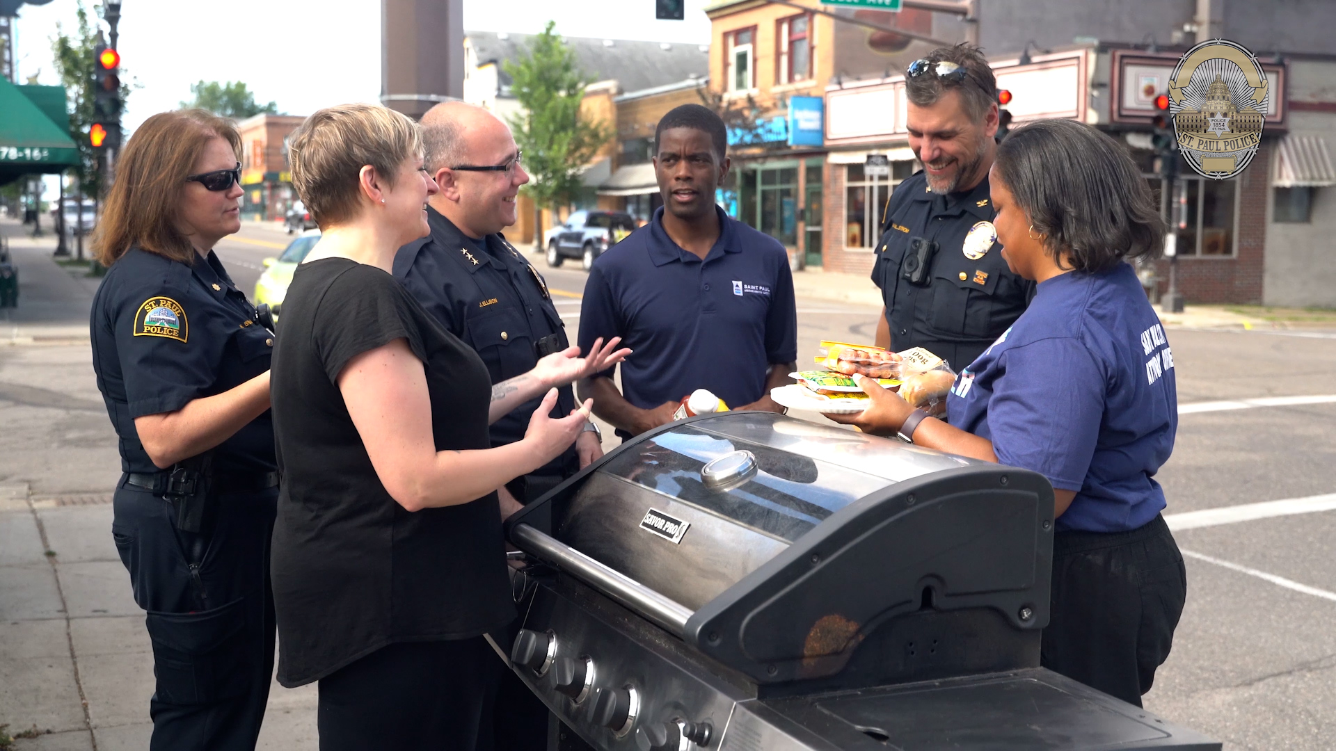 Mayor Carter stands on a public sidewalk, grilling with police officers and city staff at a community event.