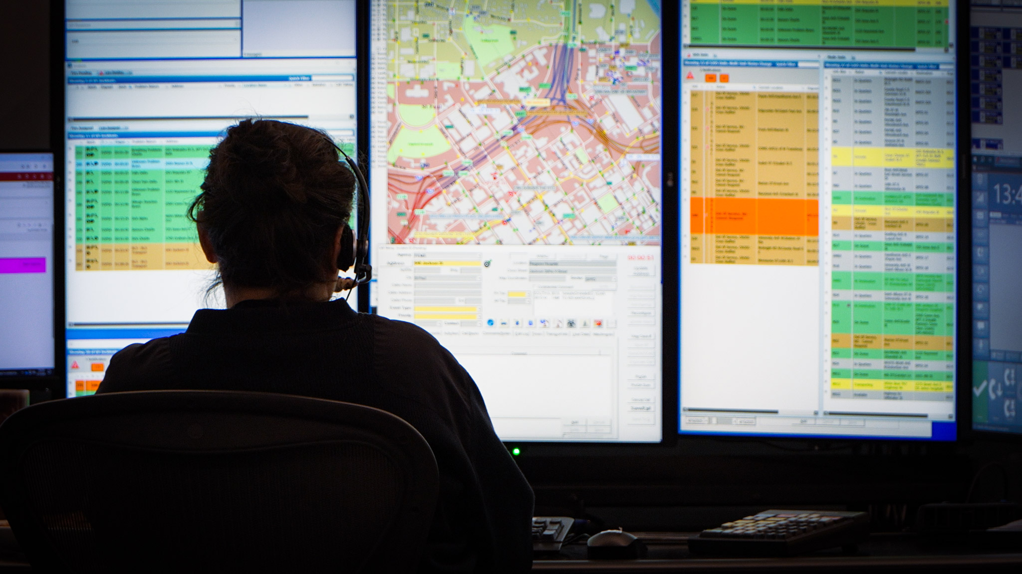 A backlit agent looks a three large monitors worth of information in a control center.