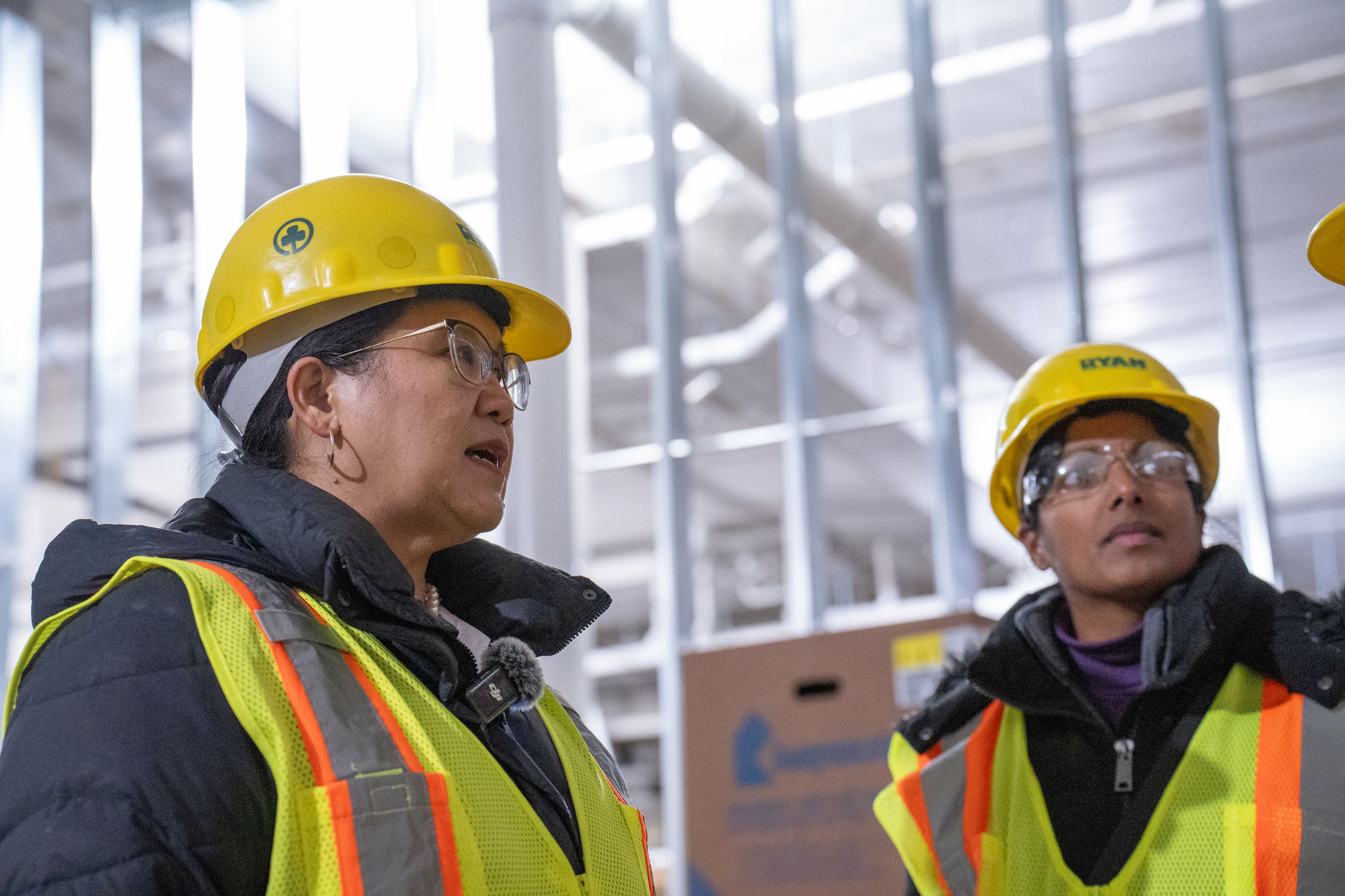Mayor Her wears a vest and hard hat in the middle of a construction site, speaking with others in vests and hard hats.