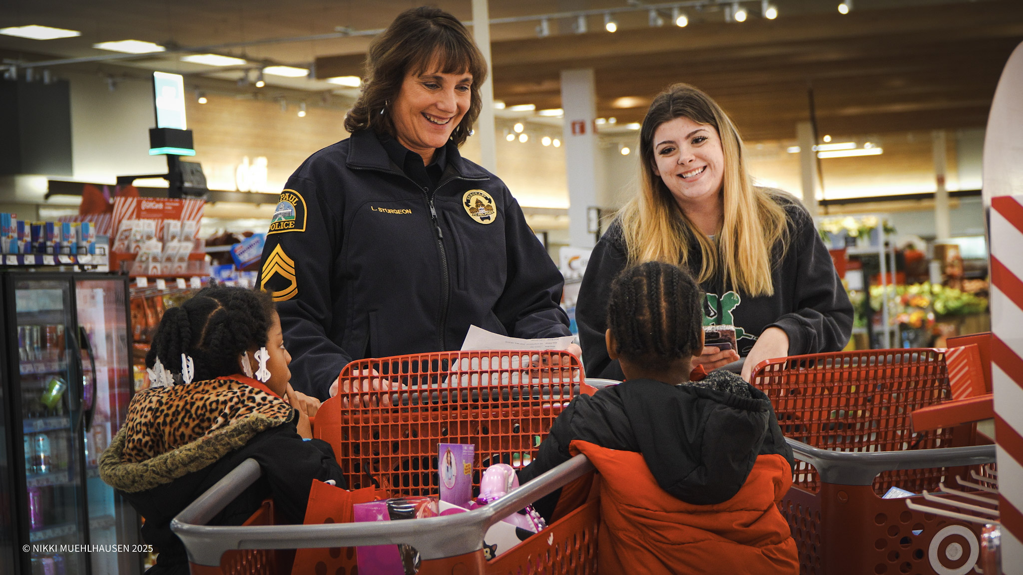 A female police officer in uniform chats with another young woman and two young children while pushing shopping carts inside of a Target store.