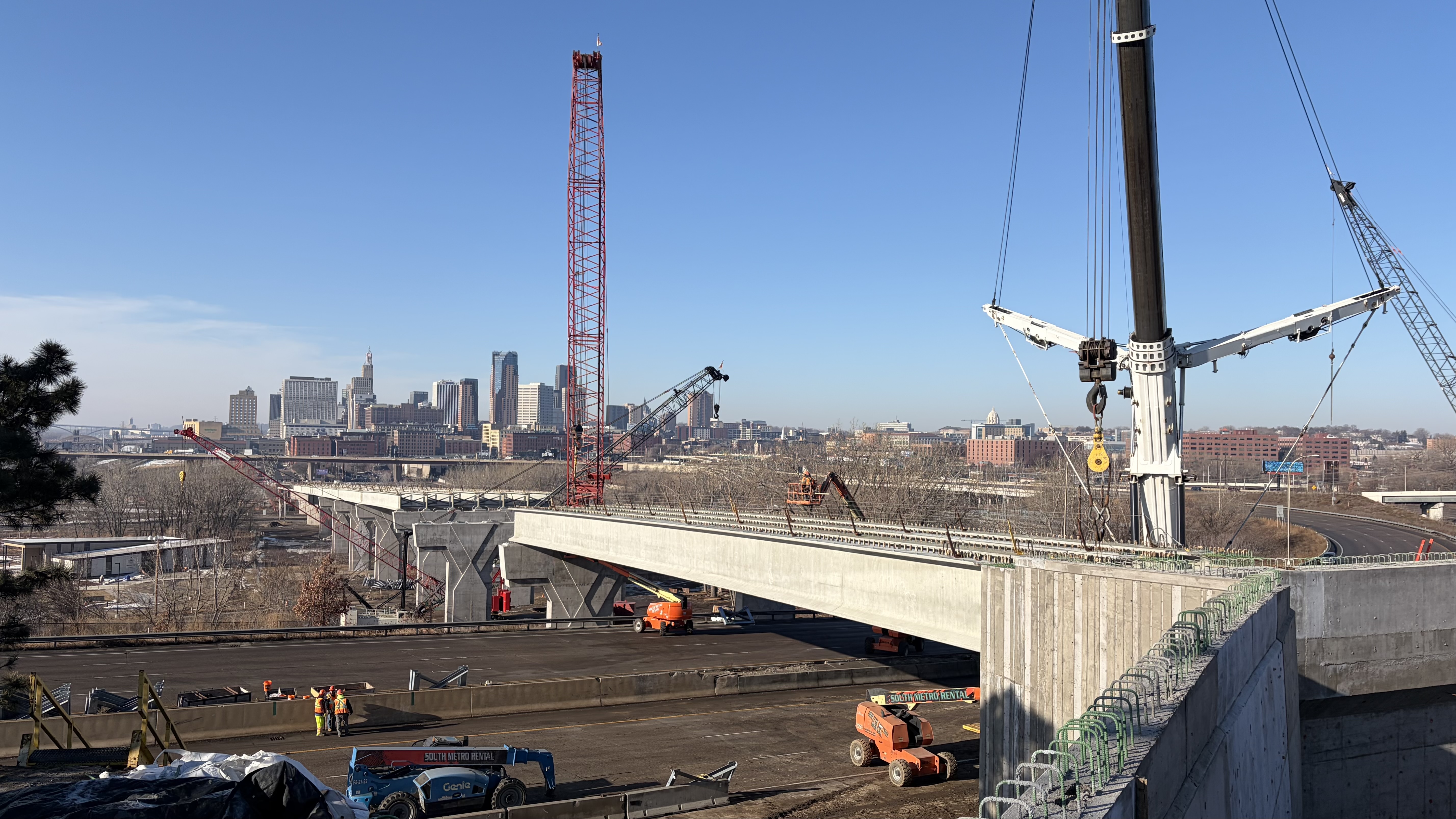 Photo showing the new beams for the Kellogg-3rd Street bridge over I-94 with large cranes and the downtown Saint Paul skyline in the background