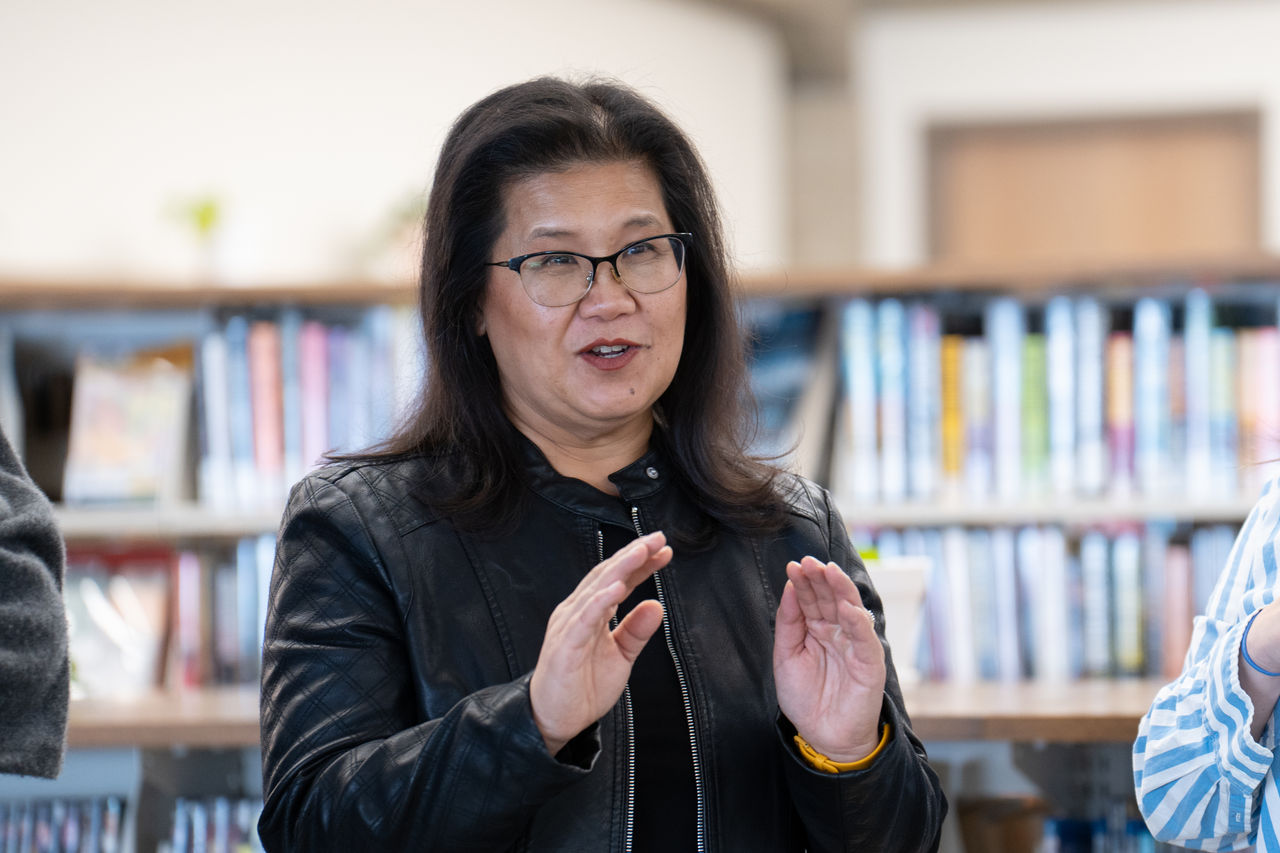 Mayor Her stands inside a library talking with a group of people.