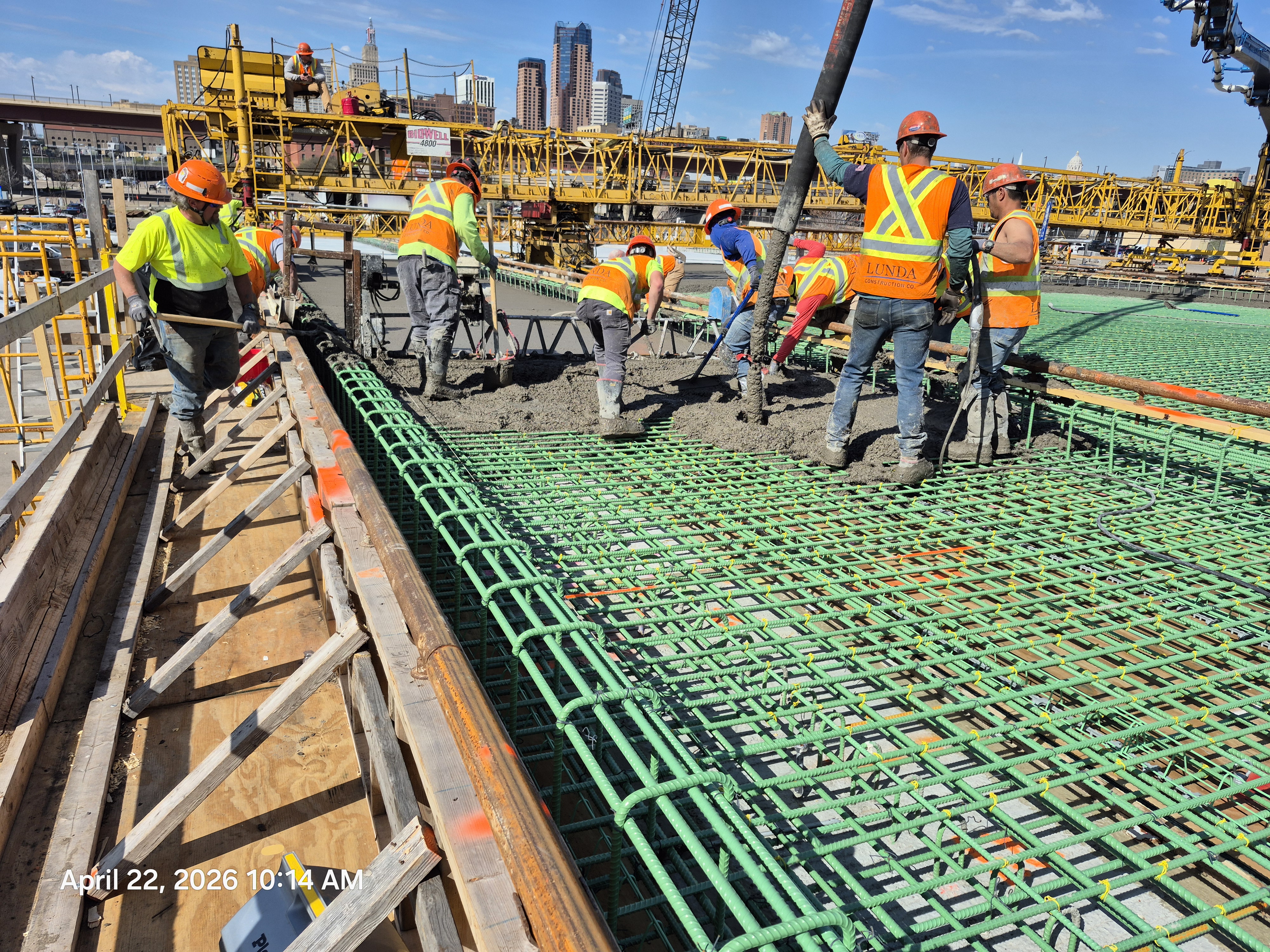 Construction crew in high visibility vests spreading concrete on the new Kellogg-3rd Street bridge on April 22, 2026.
