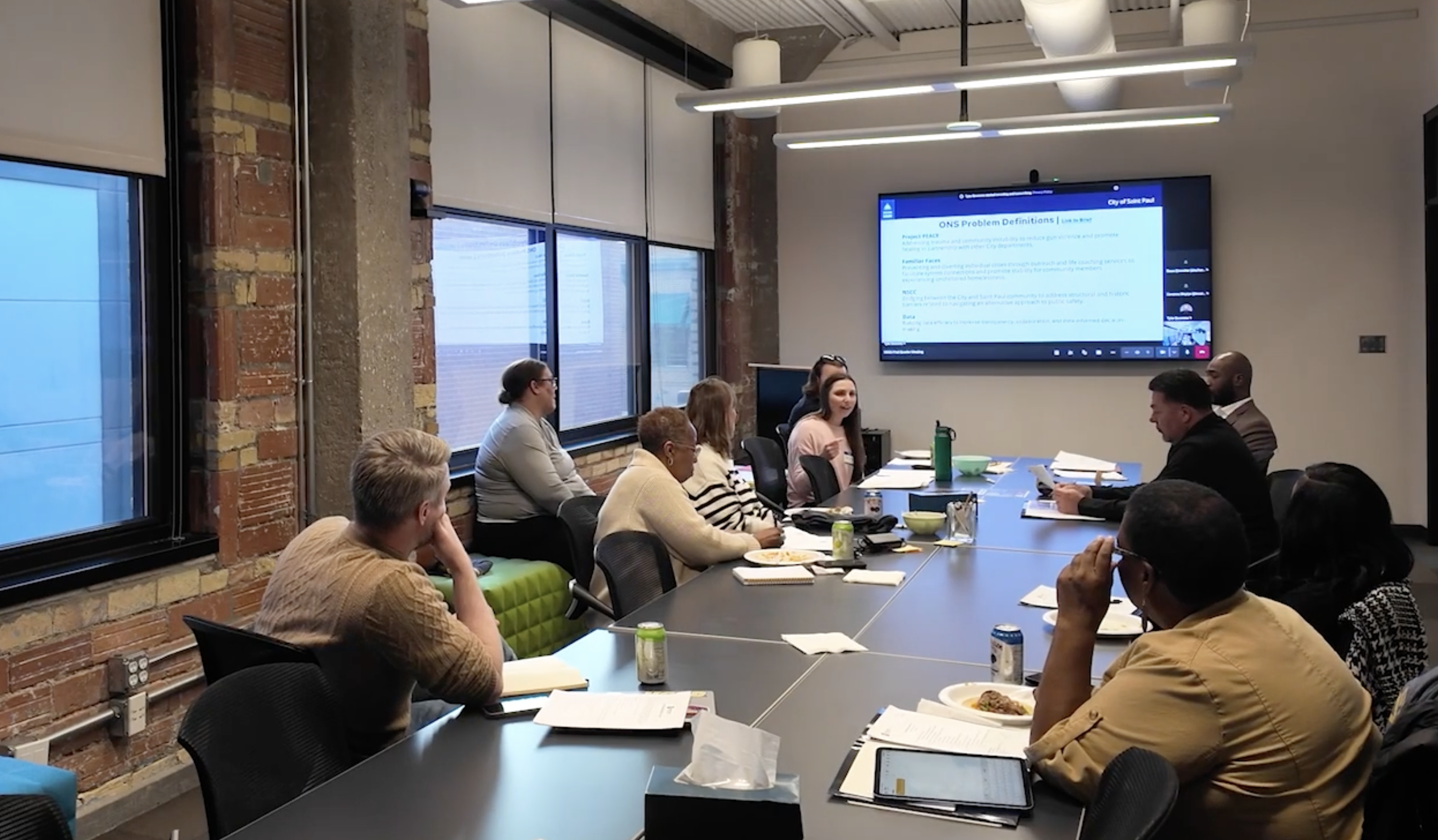 Ten people sit around a conference table with papers in front of them, talking.
