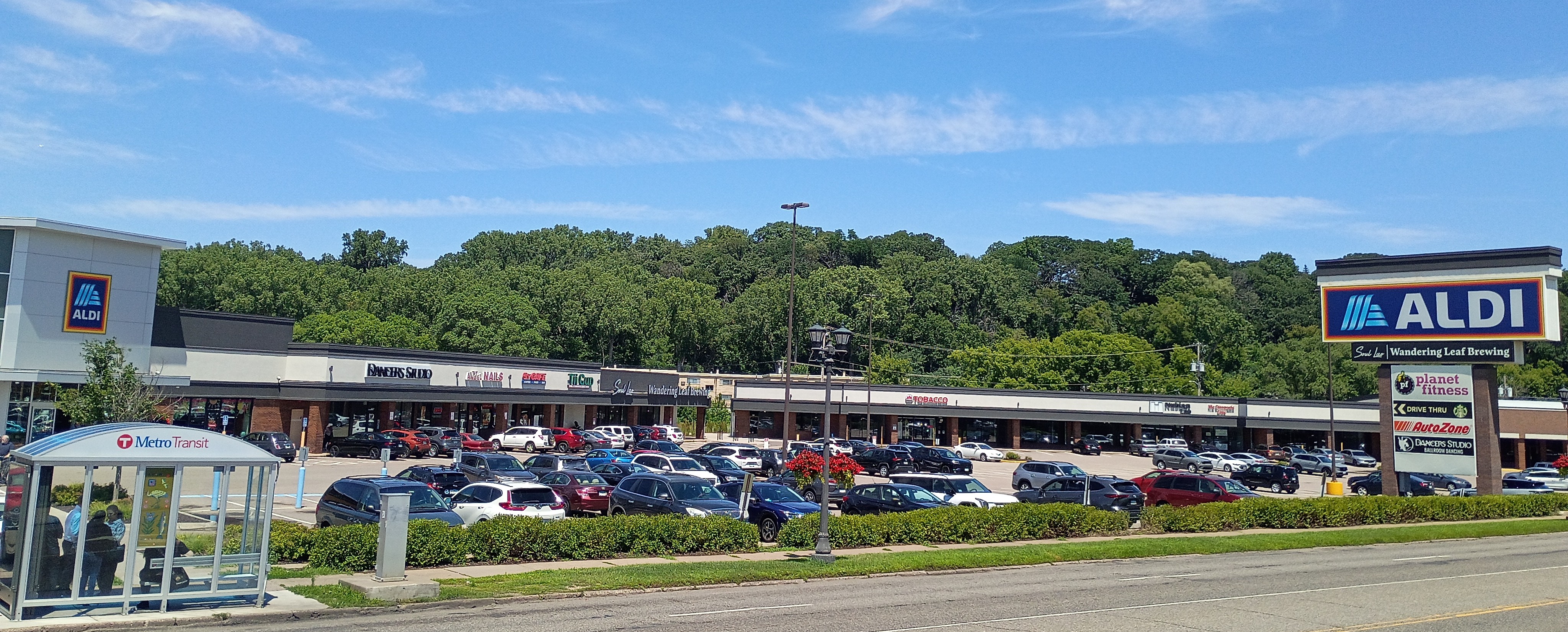 Shopping center on West 7th Street with Aldi, Dancers Studio, and other businesses, with a Metro Transit shelter in the foreground.