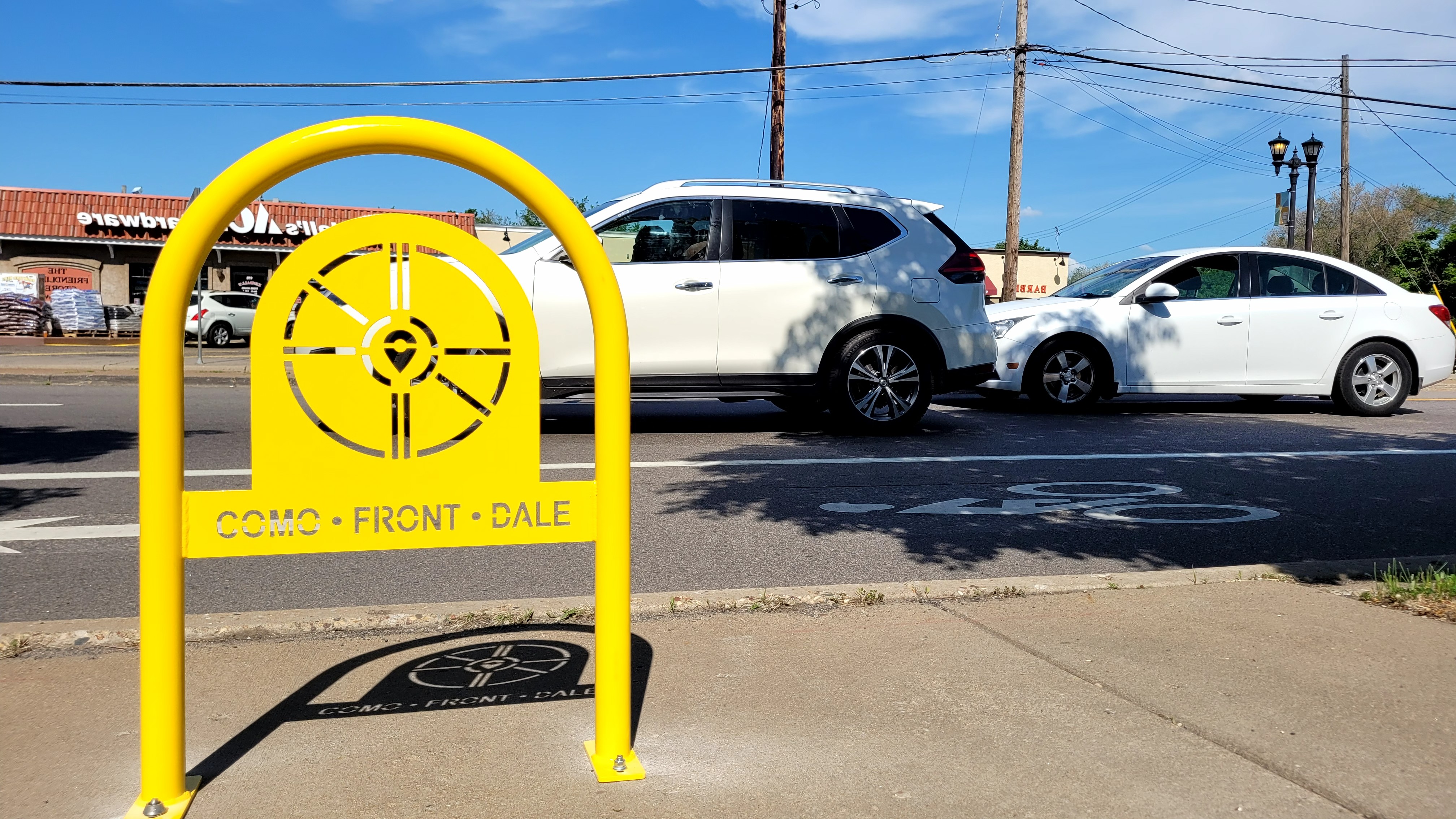 Yellow "Como • Front • Dale" bike rack on a sidewalk next to a bike lane.