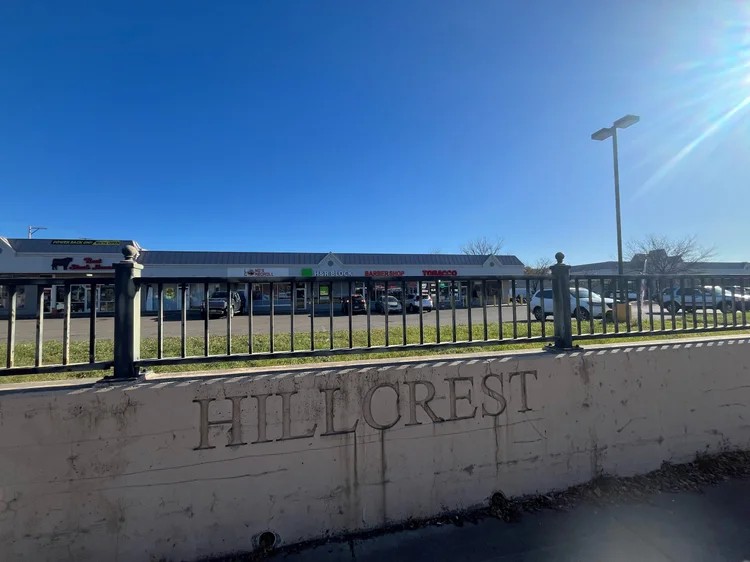 Concrete wall engraved with "Hillcrest" in front of the Hillcrest Center shopping plaza and its small businesses.