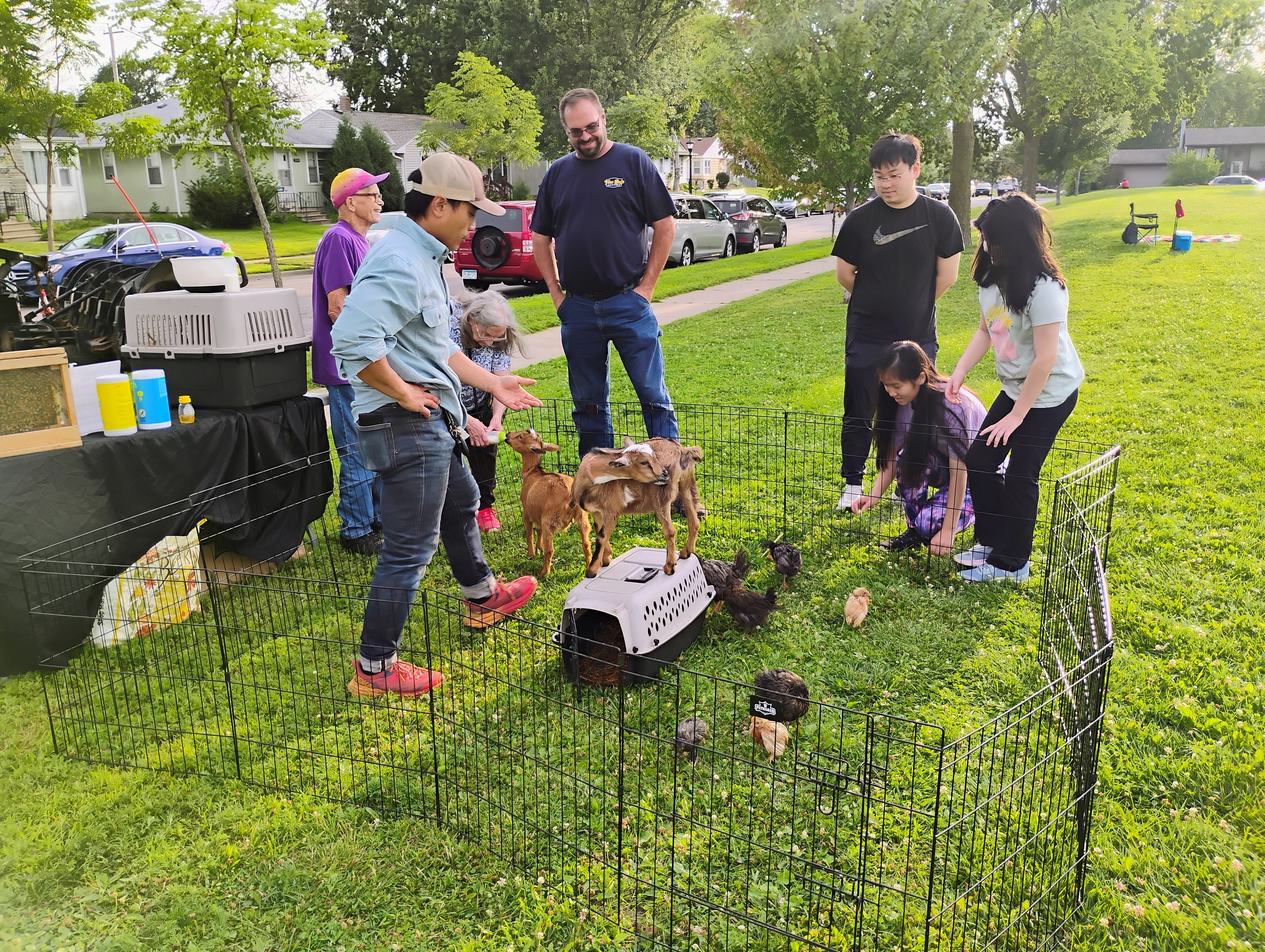 Neighbors visit a petting zoo with baby goats and chickens at a National Night Out event.