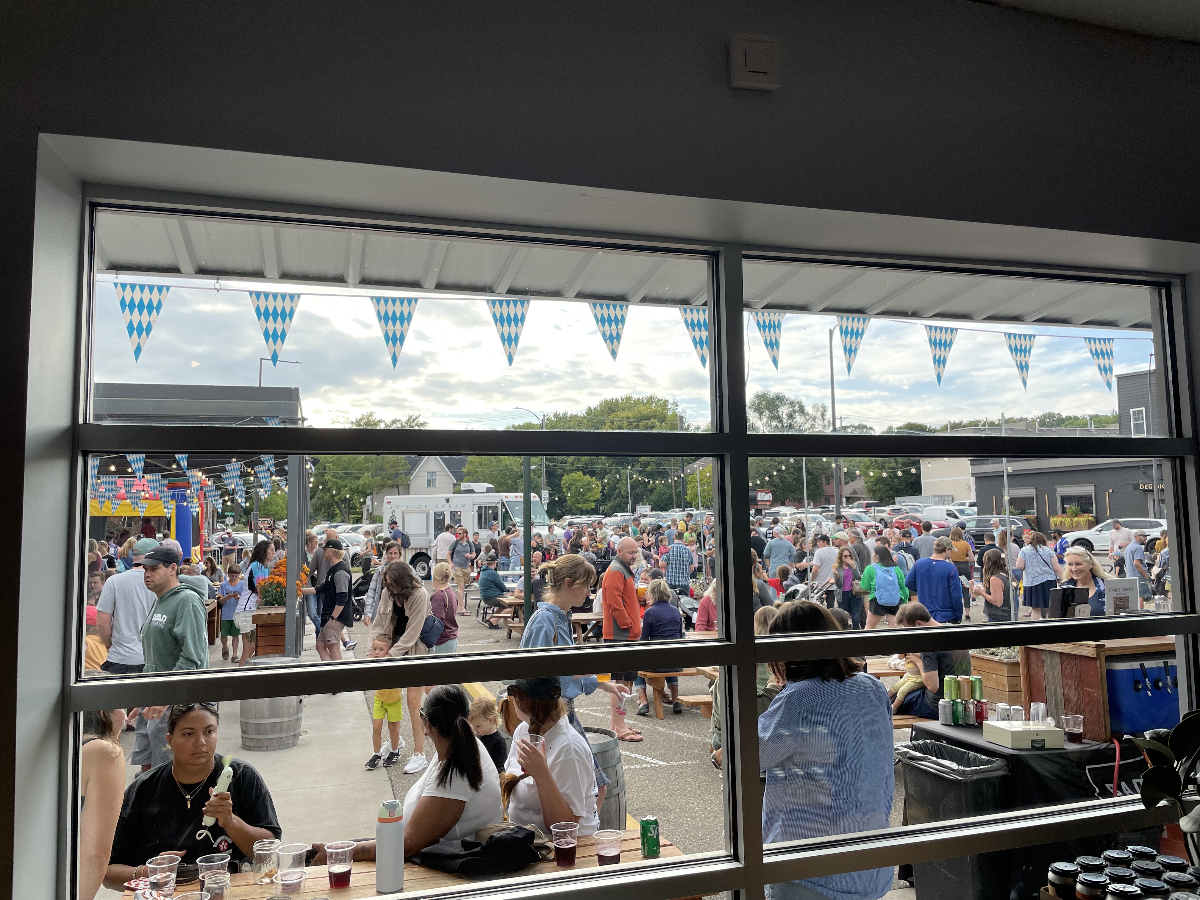 A large crowd fills the Bad Weather Brewing patio during Croctoberfest, seen through the taproom windows with Bavarian pennants overhead.