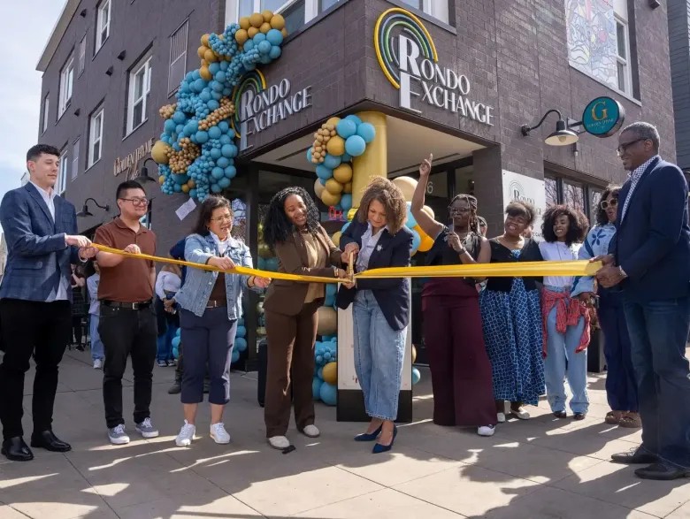Ribbon cutting at the grand opening of the Rondo Exchange, with a balloon arch framing the building's corner entrance.