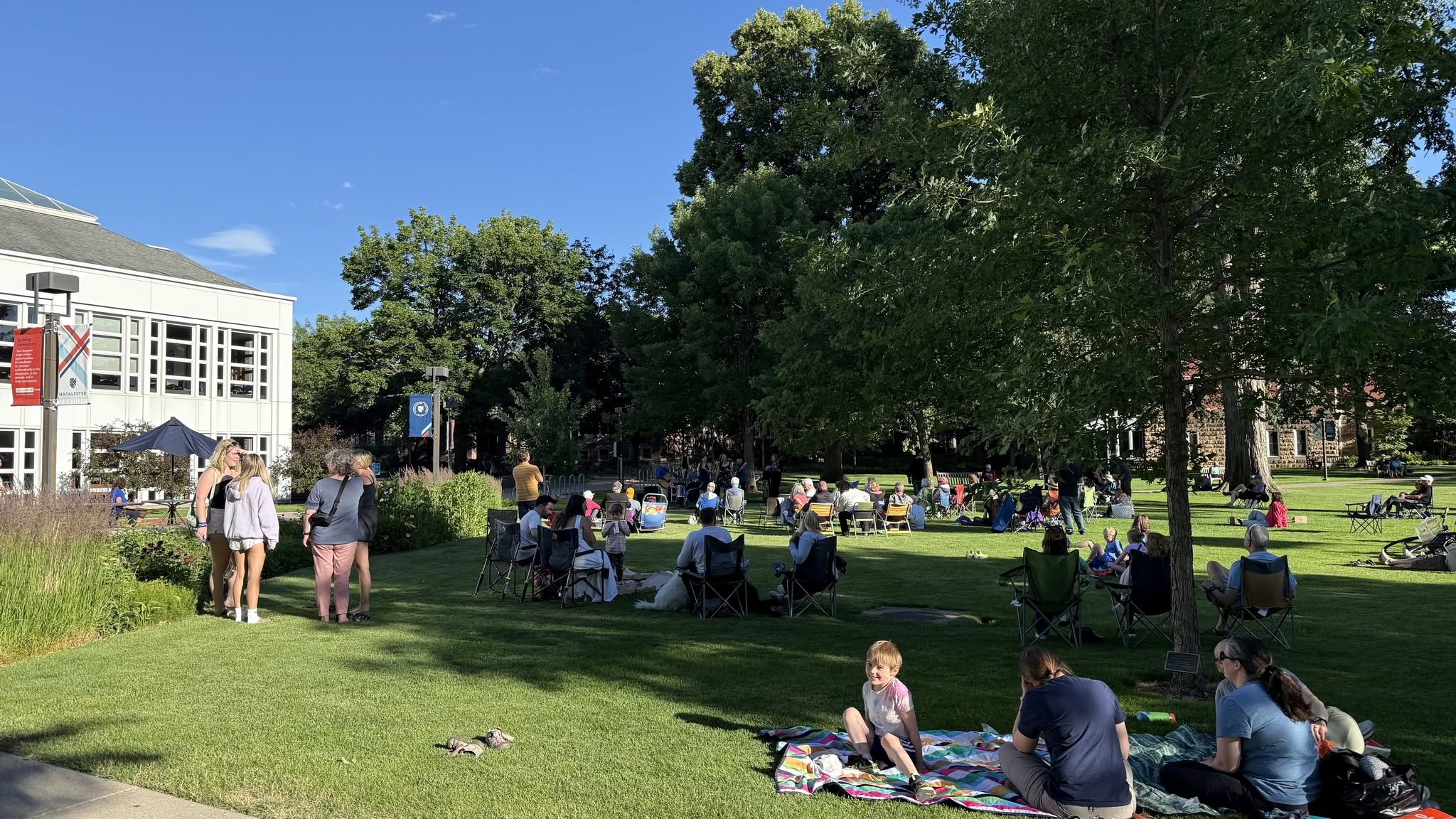 A crowd relaxes on the lawn at Grand Ave Music on the Lawn at Macalester College on a summer evening.
