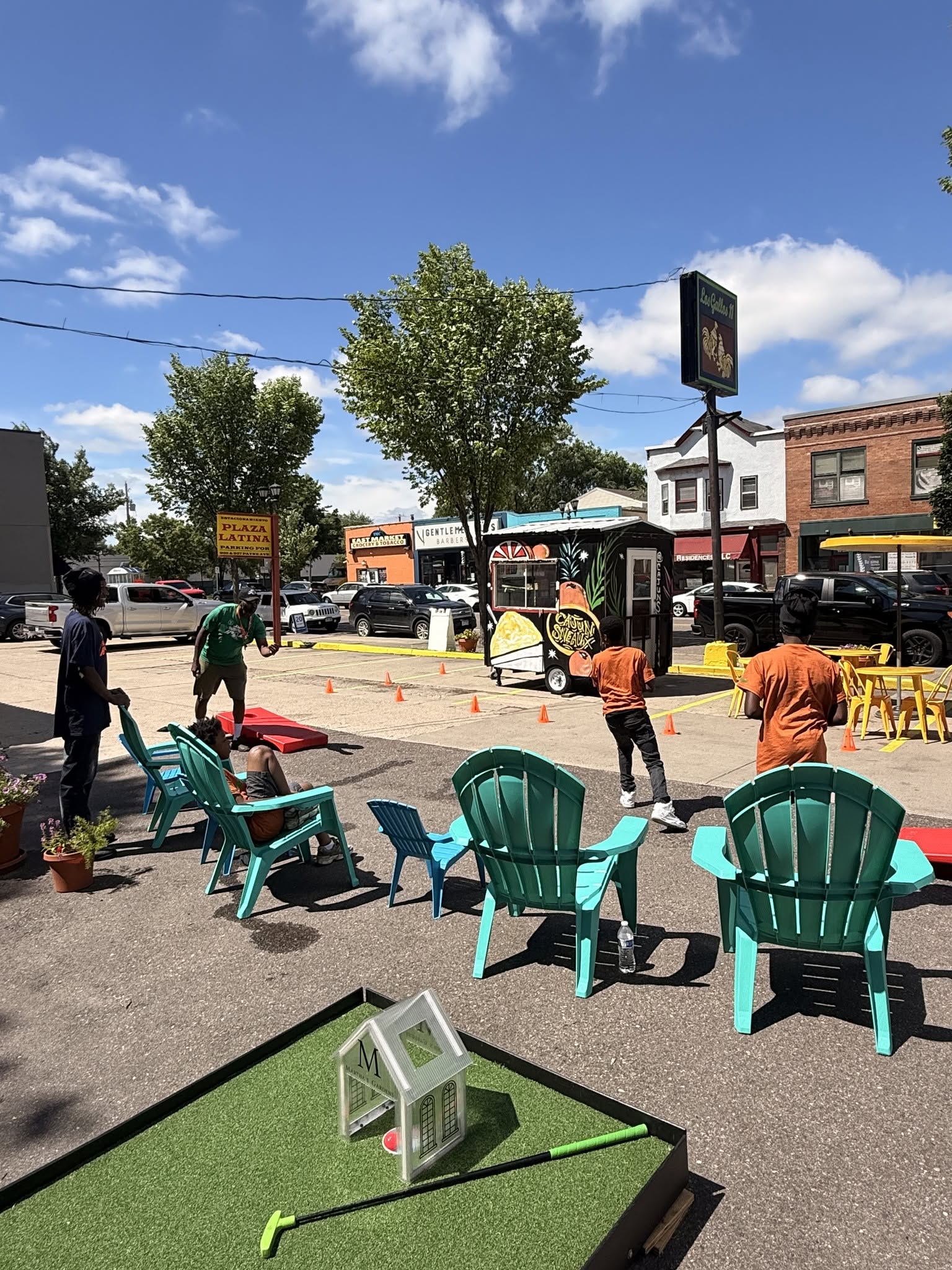A row of lawn chairs next to a mini golf course with a group of people playing cornhole.