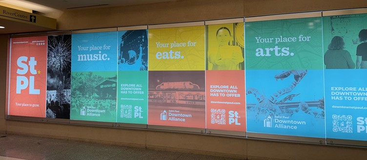 Photo of Saint Paul Downtown Alliance ad panels installed in a tunnel near the RiverCentre, with "Your place for grow / music / eats / arts" messages and downtownstpaul.com.