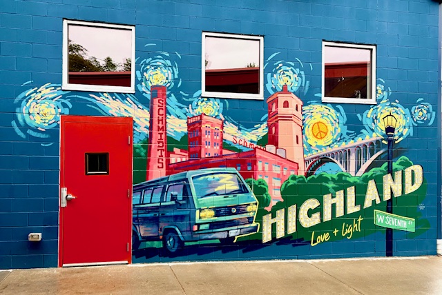 Corridor mural on the blue cinder-block wall of VanGo Automotive, depicting the Schmidt Brewery, a green Volkswagen van, and a bridge beneath a swirling Van Gogh-style starry sky, with hand-lettered text reading "Highland, Love + Light" and a West Seventh Street sign.