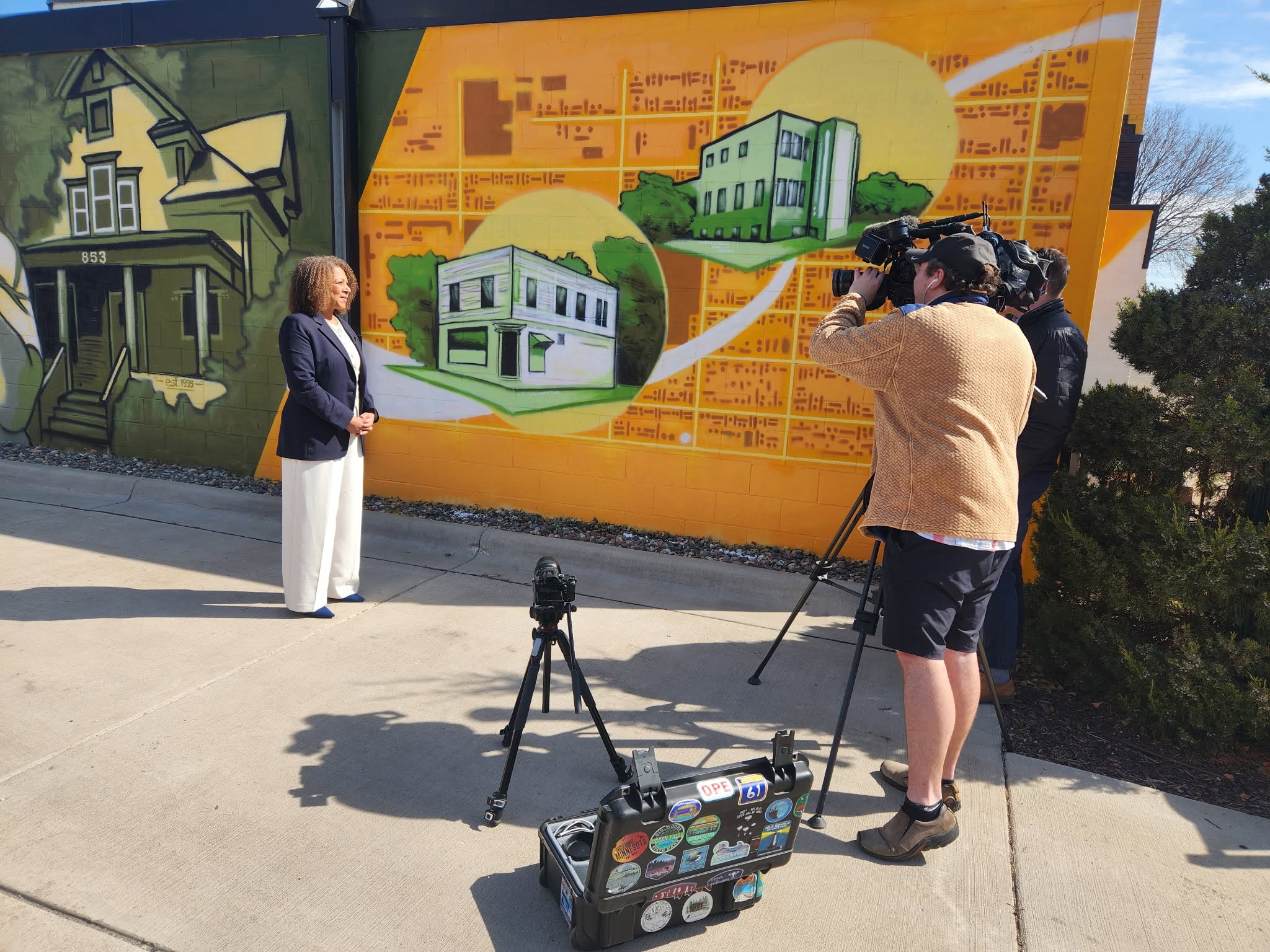 A videographer films an interview in front of a Rondo neighborhood mural.