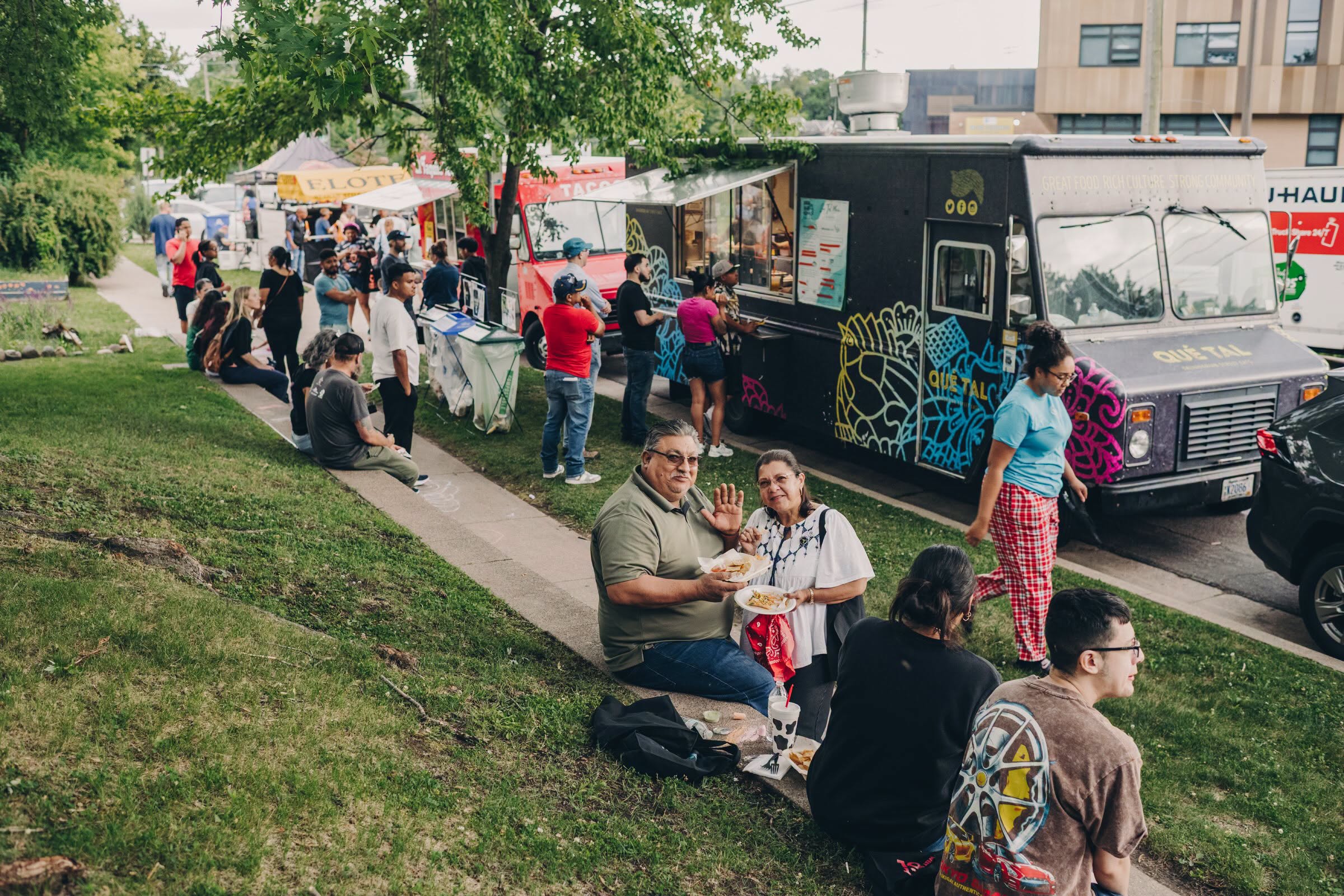 People eat and gather among food trucks at a West Side Voices community event on a summer evening.