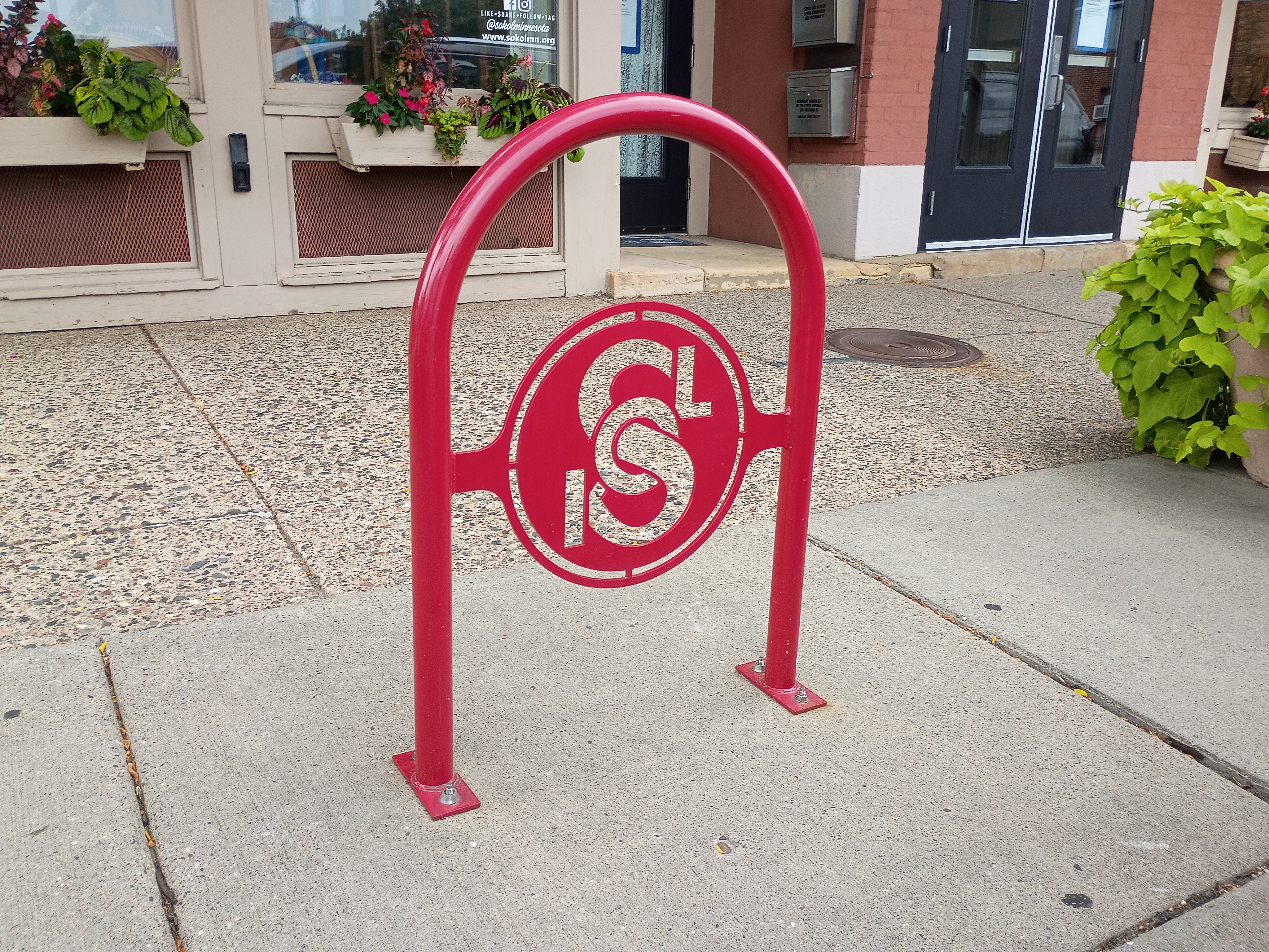 Red bike rack with a Fort Road Federation medallion installed on a West 7th Street sidewalk in front of the historic building.