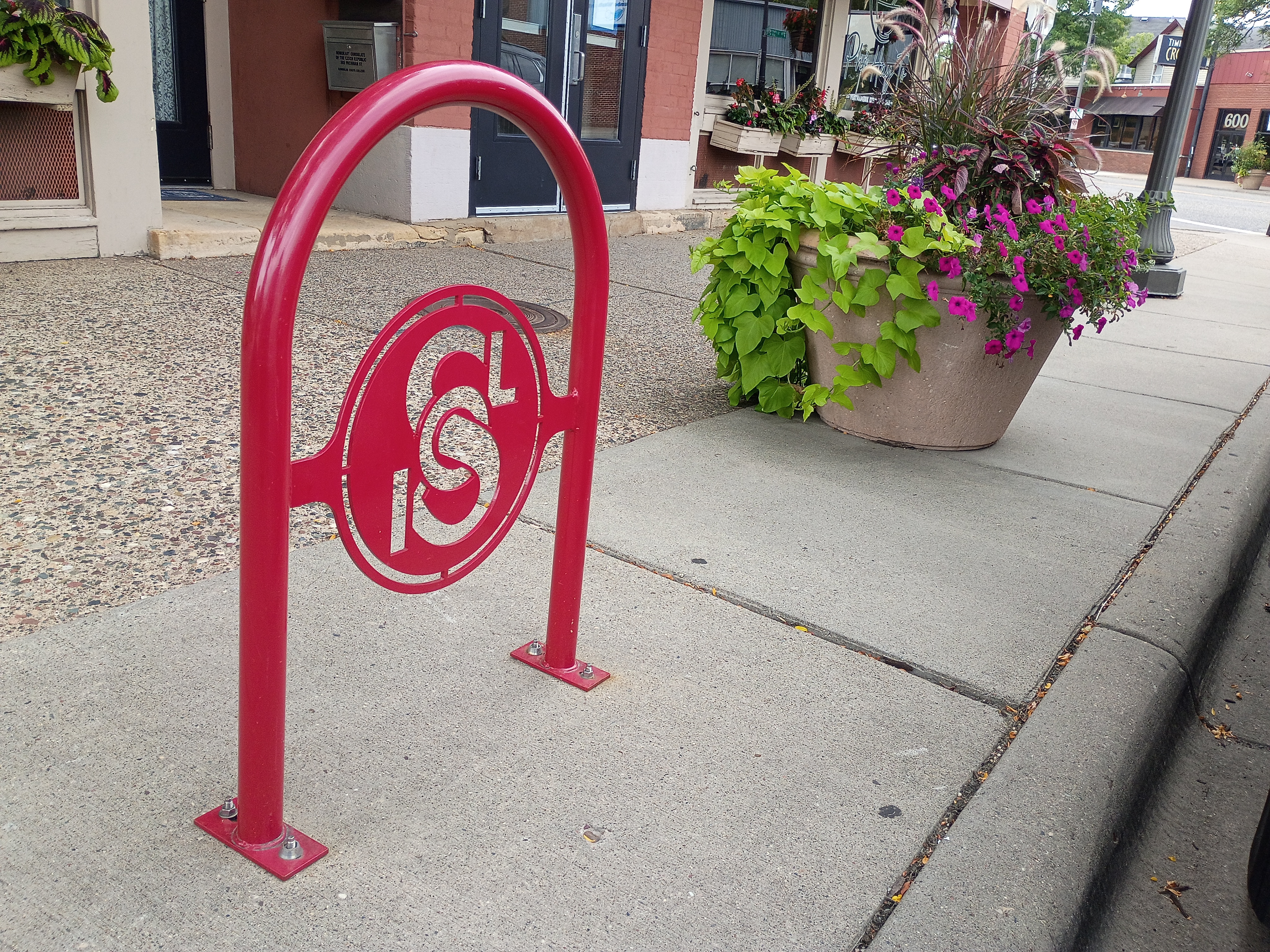Fort Road Federation bike rack on West 7th Street, viewed from a wider-angle showing planters and neighboring buildings.