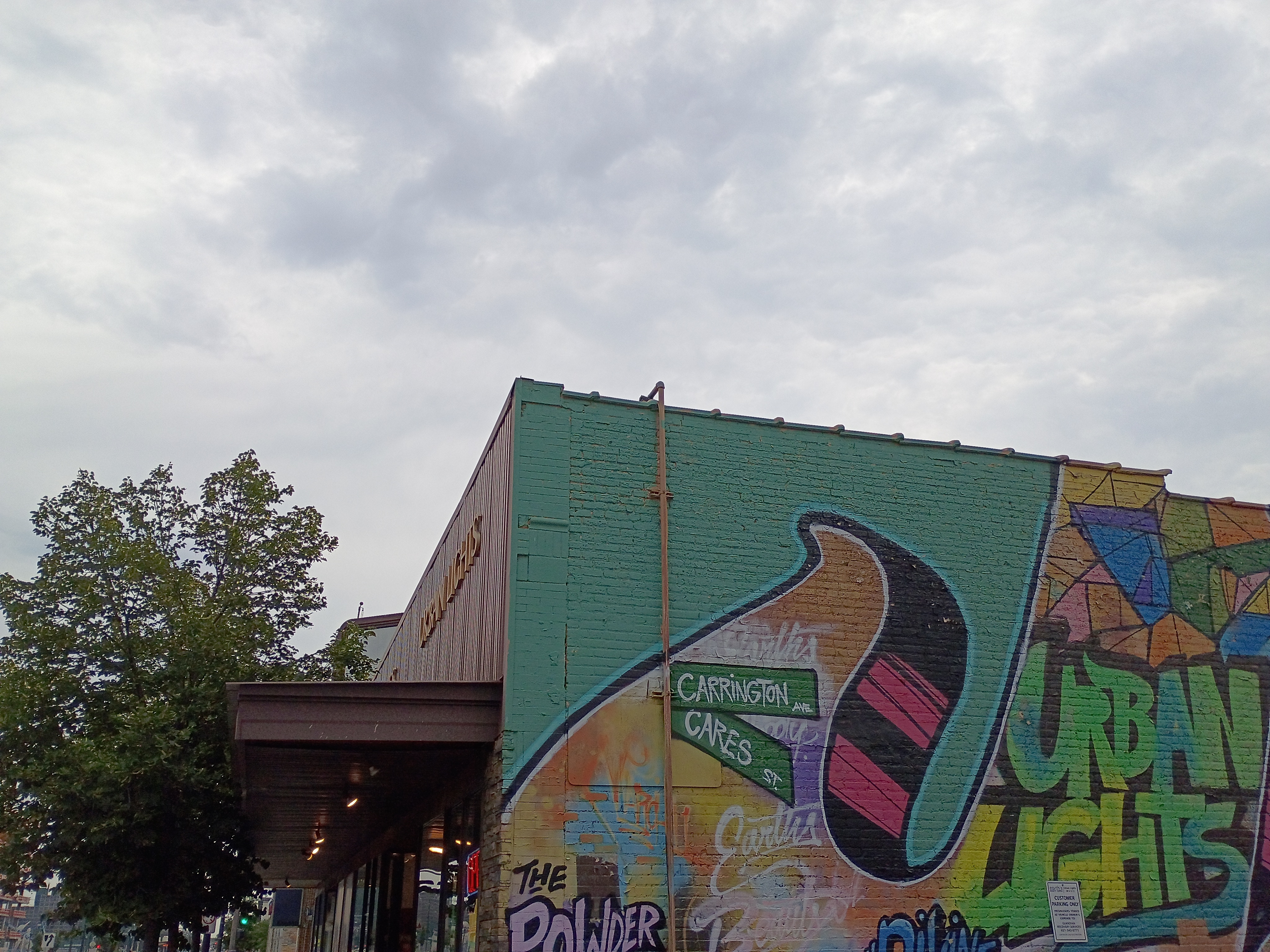 Urban Lights side-wall mural featuring bright green background, geometric shapes, stylized wings, and text elements including "Urban Lights" and "Carrington Ave / Cares St."