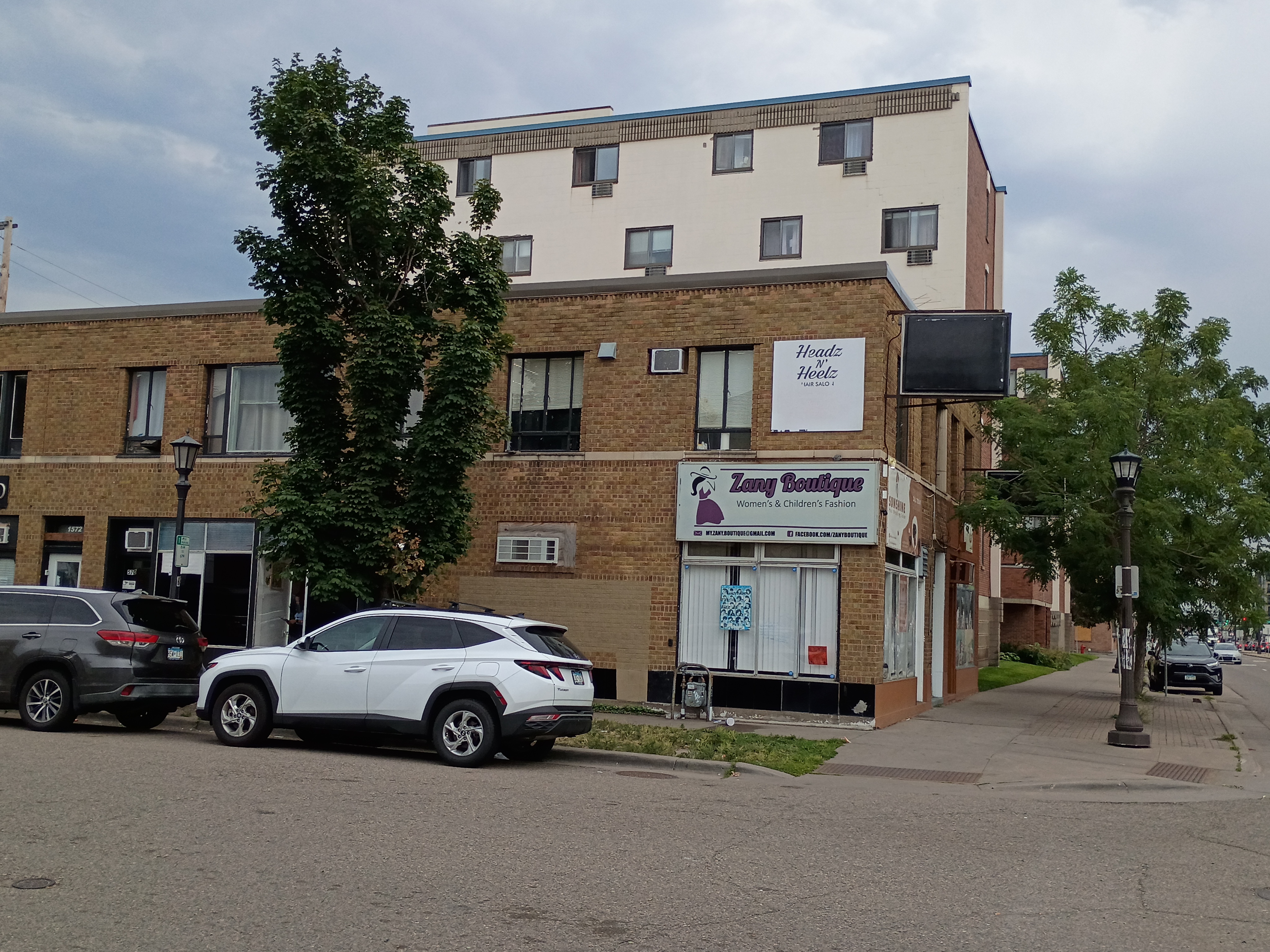 Row of University Avenue storefronts including Headz N' Heelz Hair Salon and Zany Boutique, with additional businesses along a tan brick building.