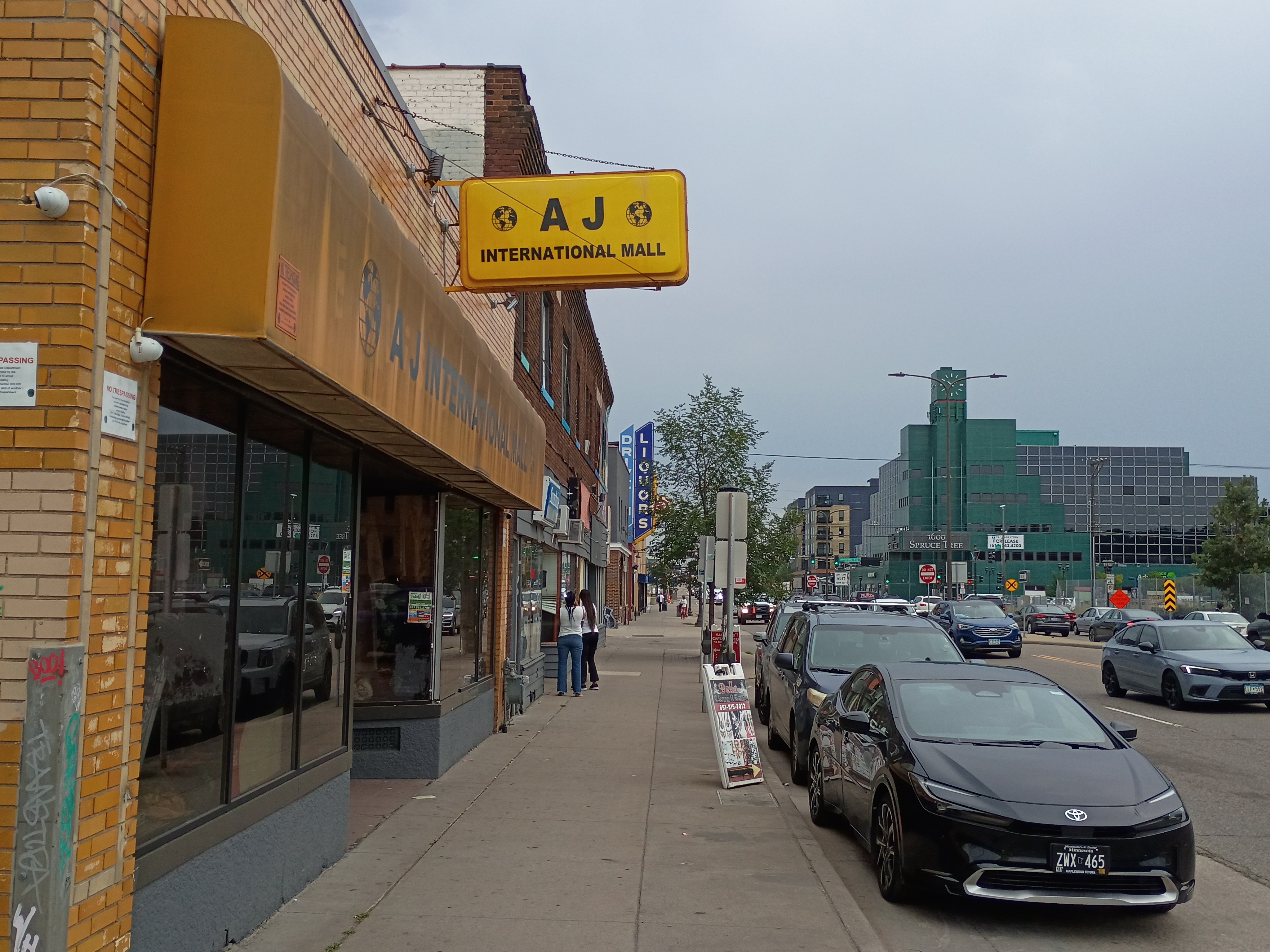 AJ International Mall storefront on University Avenue with its yellow sign and awning, with the Spruce Tree Centre visible in the background.