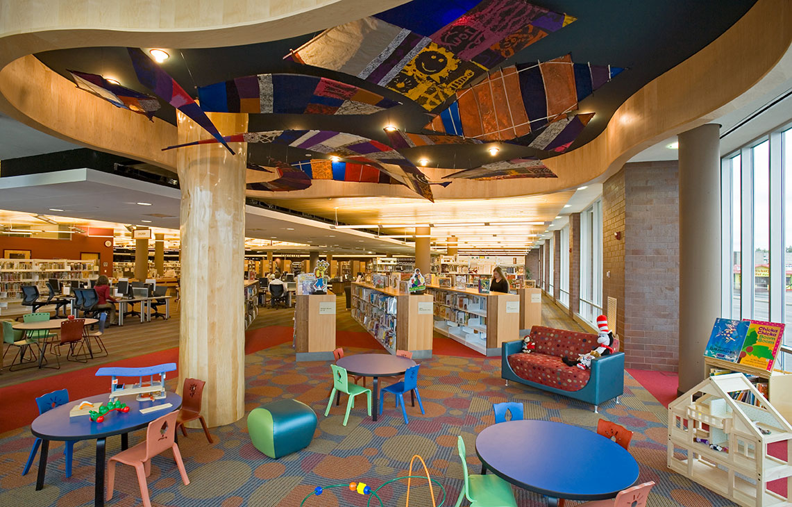 Interior of the Rondo Community Library's children's area, with colorful tables and chairs beneath a curved ceiling installation of hanging quilt panels.