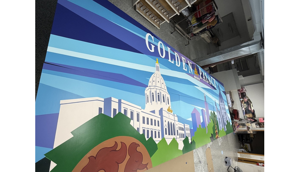 The Golden Palace mural nearly complete in a workspace, showing the wordmark and Saint Paul skyline elements against a blue geometric sky.
