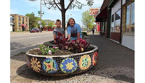 Two children stand behind a mosaic-tiled sidewalk planter filled with flowers on Snelling Avenue, with the Snelling Cafe sign visible in the background.