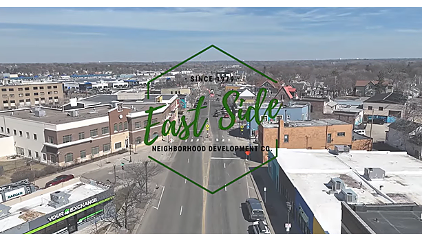 East Side Neighborhood Development Co. logo overlaid on an aerial view down an East Side Saint Paul commercial corridor, with brick storefronts and residential blocks extending to the horizon.