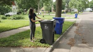 Picture of a woman placing a garbage cart out at the curb.
