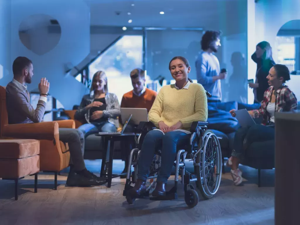 Portrait of disabled businesswoman in a wheelchair in front of her diverse business team at office 