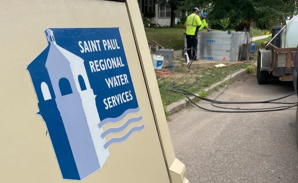 Saint Paul Regional Water Services equipment near workers in safety vests performing maintenance on a residential street lined with trees.