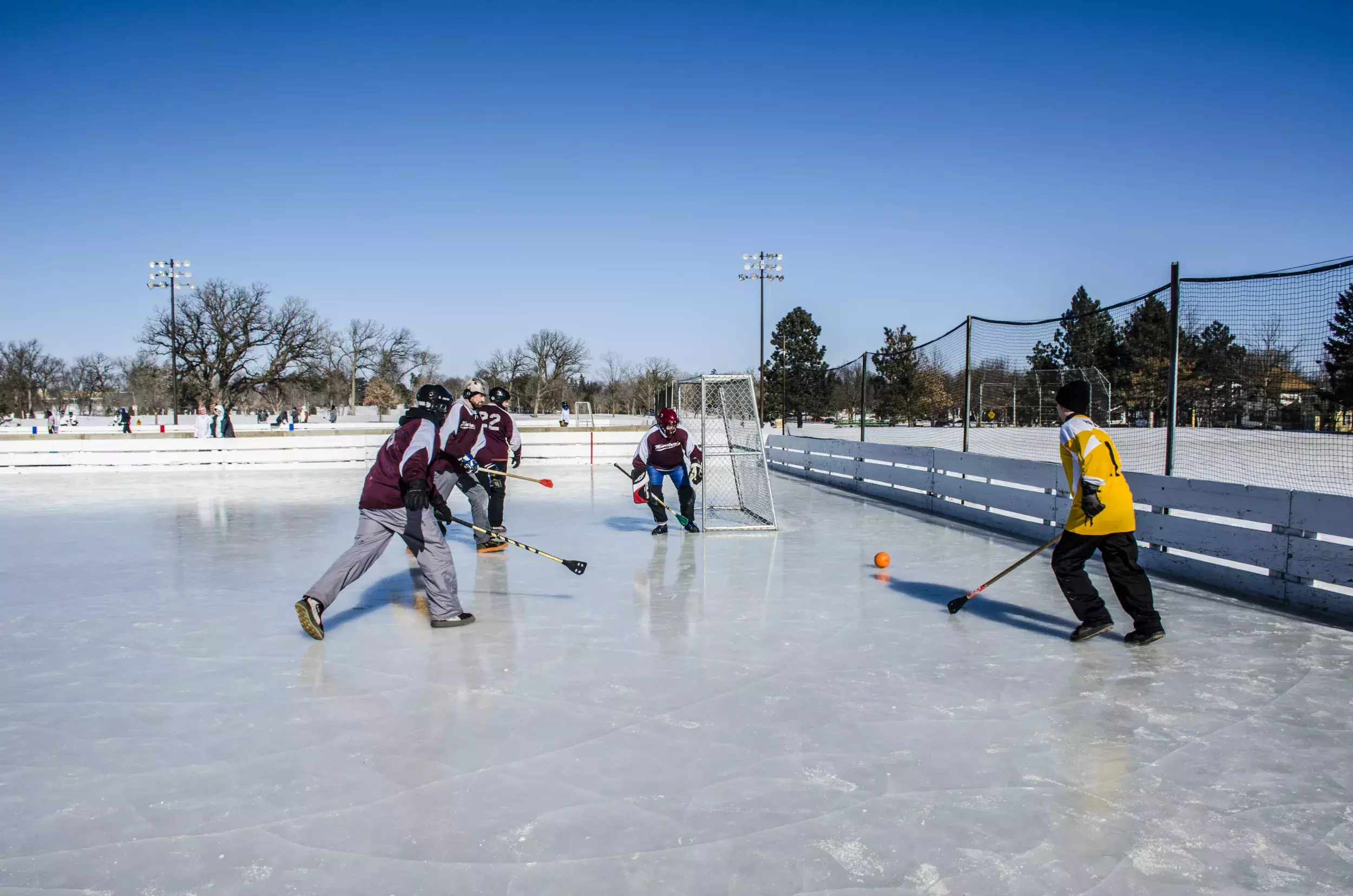 Adults playing broomball on an outdoor ice rink. 