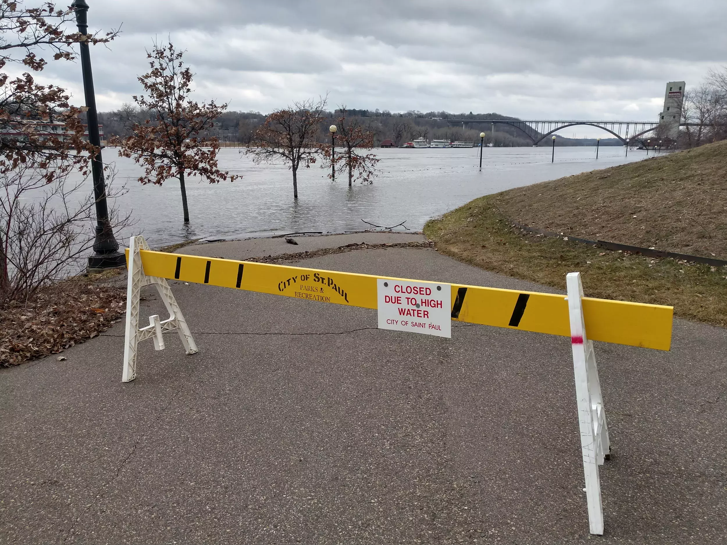 Photo from 2019 flood of a sawhorse barrier closing a trail along the Mississippi River in St. Paul