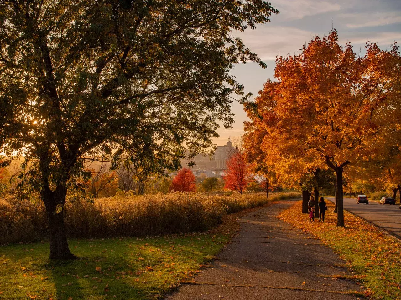 A family walks along Mounds Park surrounded by trees with autumn colors and a view of downtown Saint Paul.