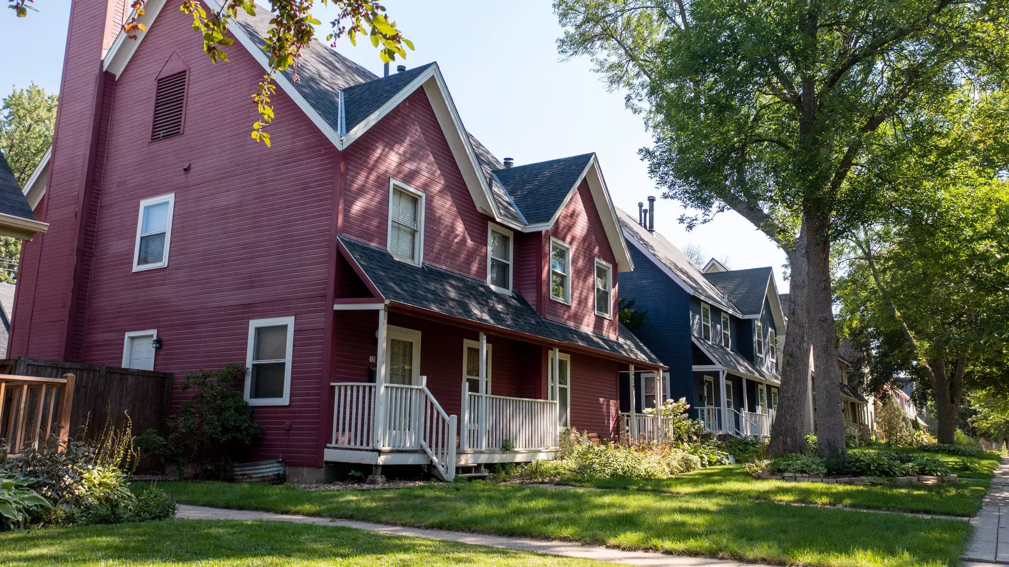 Red row house on a residential street with front yard and trees. 