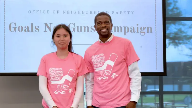 On August 5, 2025, Hser Wah and Mayor Carter wear Goals Not Guns tee-shirts designed by Wah. A teenager and a man stand side by side, smiling, in ping tee-shirts that say "Dispose the Guns, Not Our Bodies"