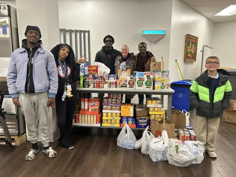 Five children and one adult smile and pose around a table piled high with pasta and canned goods.