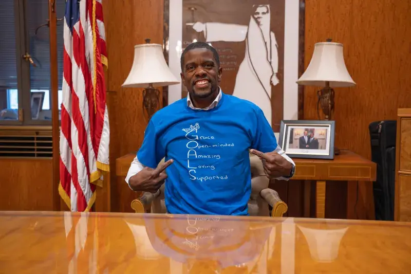 A man in a formal office models a tee-shirt that says "Grace, Open-minded, Amazing, Loving, Supported"