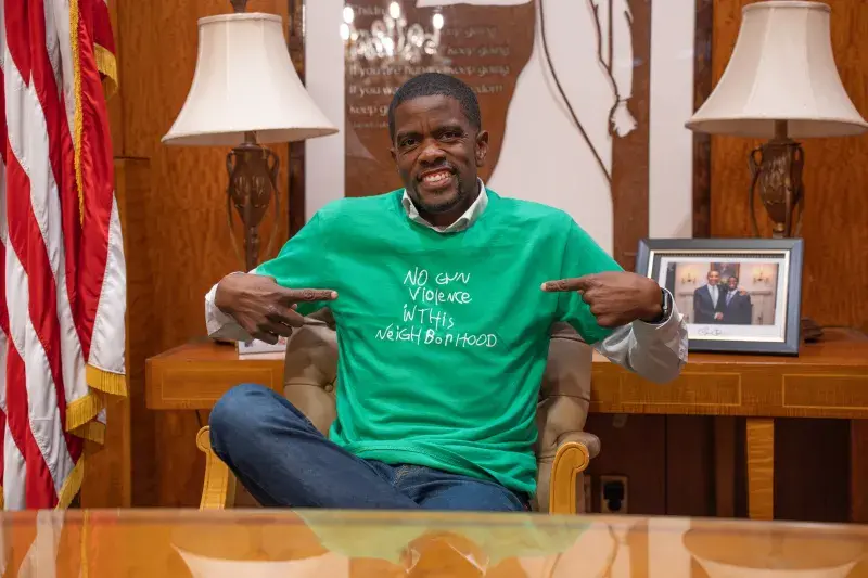 A man in a formal office models a tee-shirt that says "No Gun Violence in This Neighborhood"