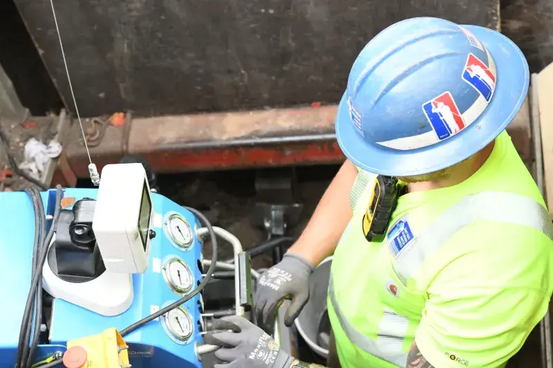 A worker guides horizontal drilling equipment underground to allow for a new copper line to be pulled through from the street to the house during a lead replacement.