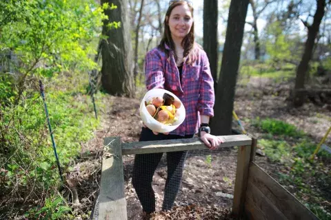 woman holding bowl with food scraps to dump into outdoor compost bin