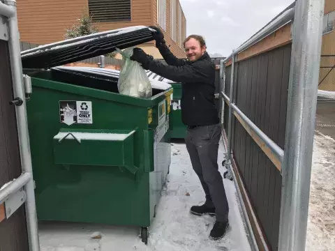 man dropping a compostable bag into a dumpster at a compost drop-off dumpster