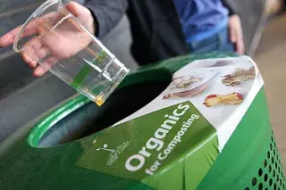 image of a hand placing a compostable cup into an organics recycling container