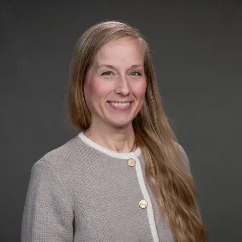 A photo of Nicole Tillander smiling warmly, her hair falling over her left shoulder, wearing a cream-colored button-up cardigan.