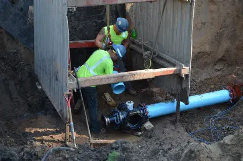 Two SPRWS workers installing water main pipes inside a trench box