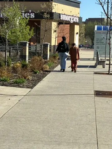 A woman and a man walk together down a city sidewalk on a sunny morning.